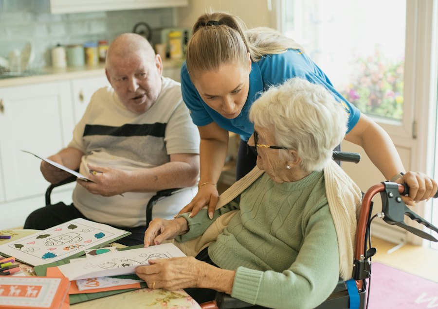 A care worker helping an older couple with a colouring activity at a kitchen table.
