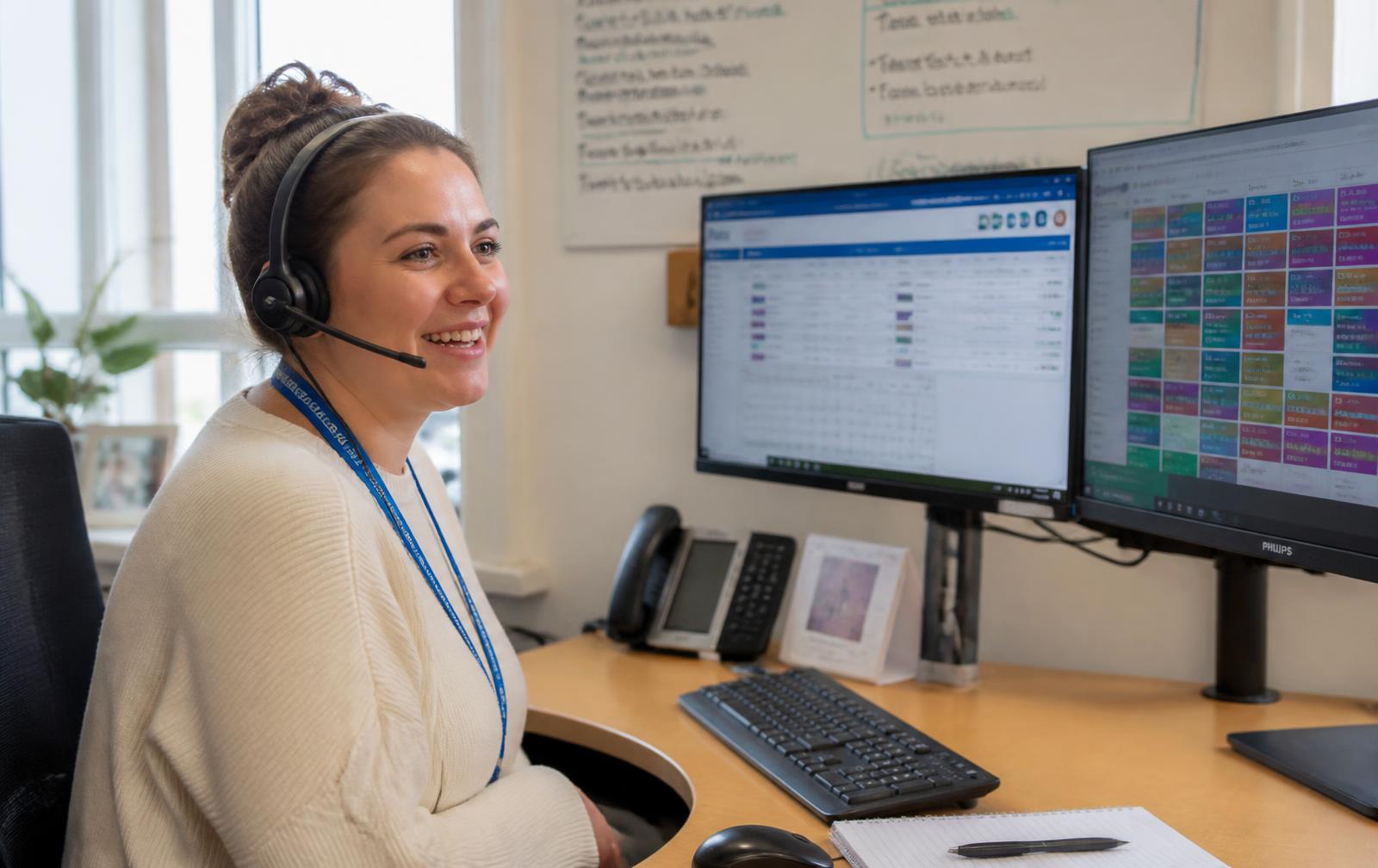 A care coordinator on a headset managing shift schedules at her desk.
