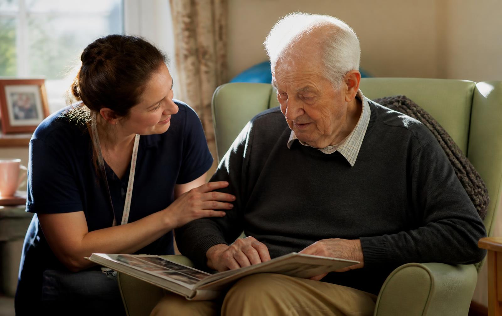 A support worker looking through a photo album with an elderly man living with dementia.